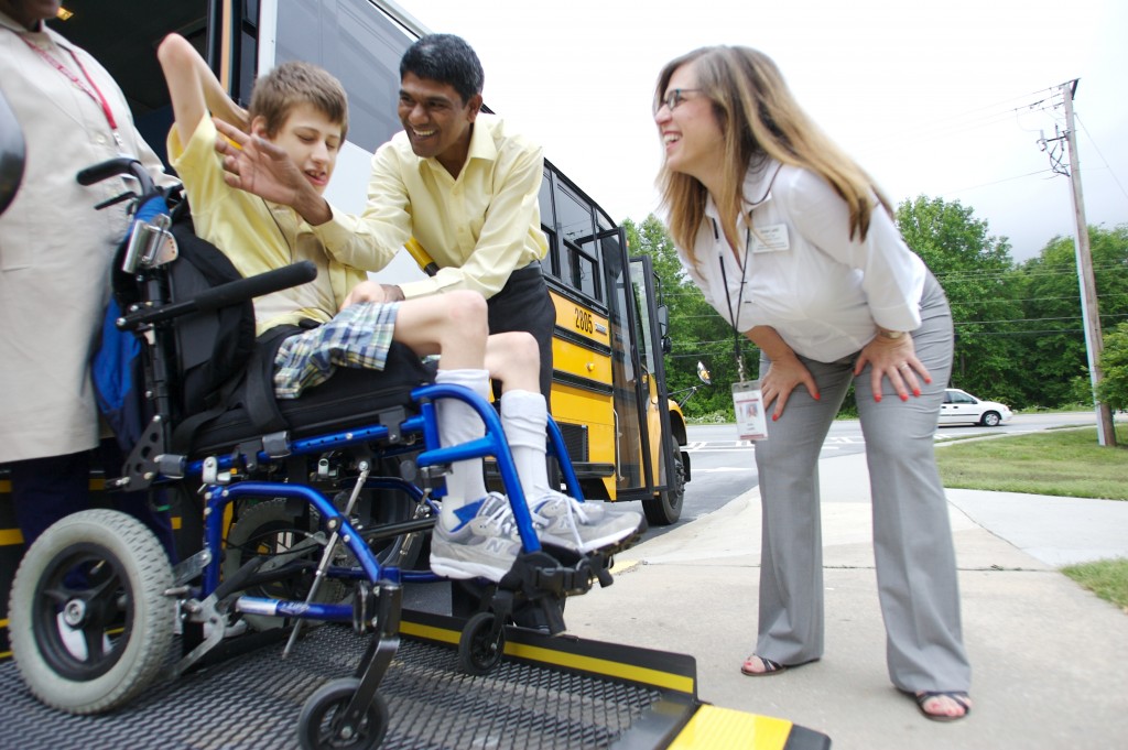 Parent watches as student in wheelchair is unloaded from bus