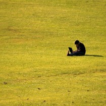 Student sitting alone in a large field studying