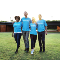 Four people wearing identical T shirts walk in a sunny field