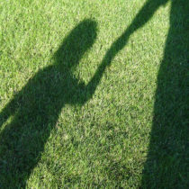 Green grass showing a shadow of a child holding a grown up's hand