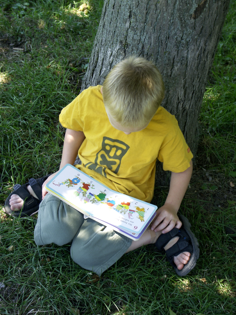 Boy sitting against tree reading