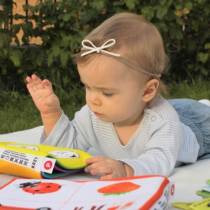 toddler laying on tummy on a blanket on the grass looking at a baby book