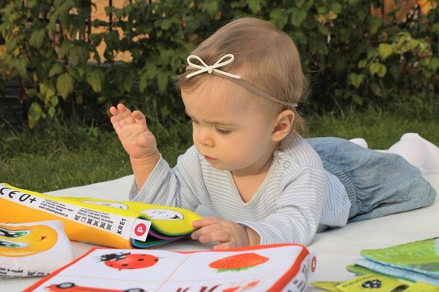 toddler laying on tummy on a blanket on the grass looking at a baby book