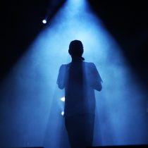 rear view of a person silhouetted on stage surrounded in blue light