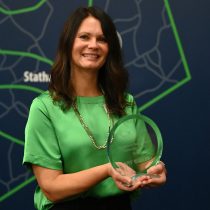 Woman stands in front of a map holding award