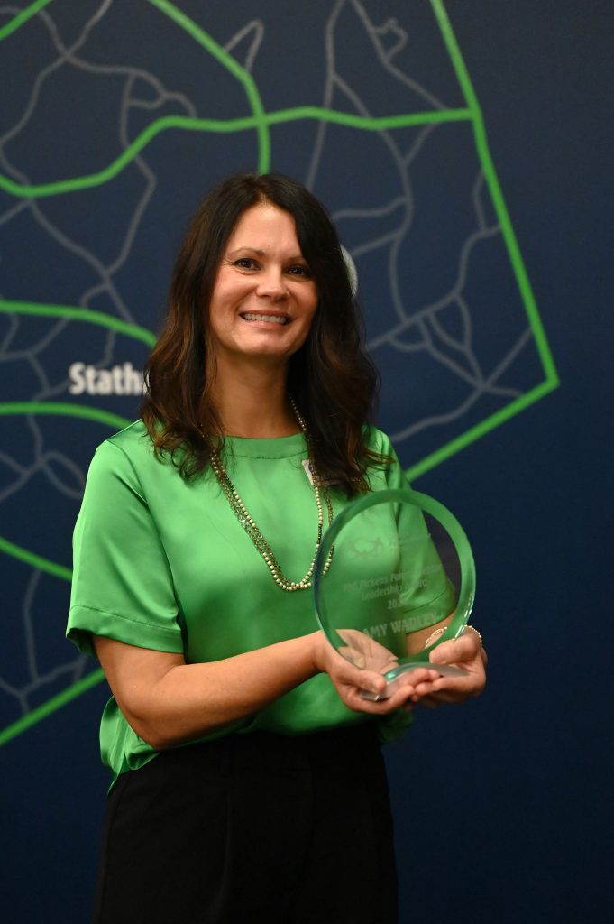 Woman stands in front of a map holding award